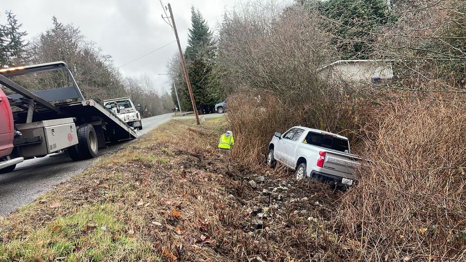 Tow trucks and a worker in a reflective jacket assisting a pickup in a roadside ditch