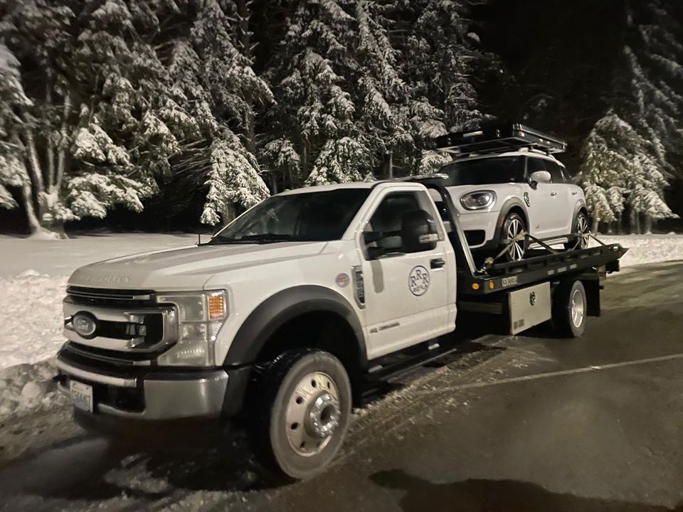 Rapid Roadside Runner flatbed carrying a white Mini beside snow-covered trees at night